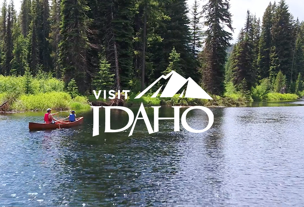 Visit Idaho logo over background of canoe in river