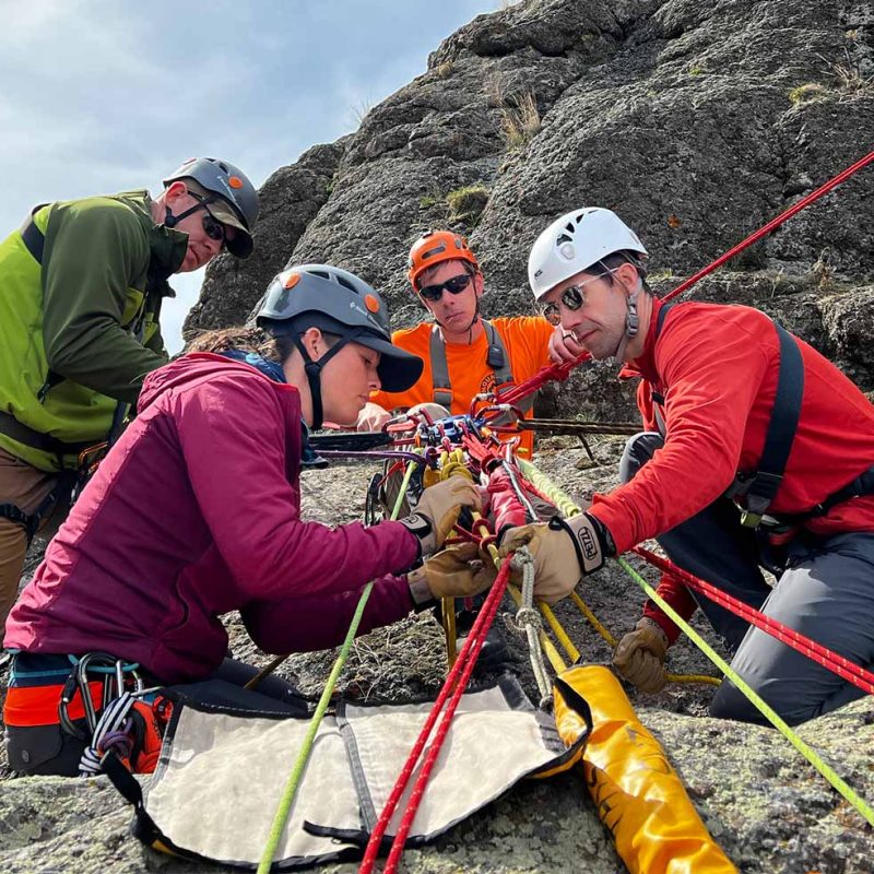 Four individuals on a rocky hillside inspecting climbing equipment